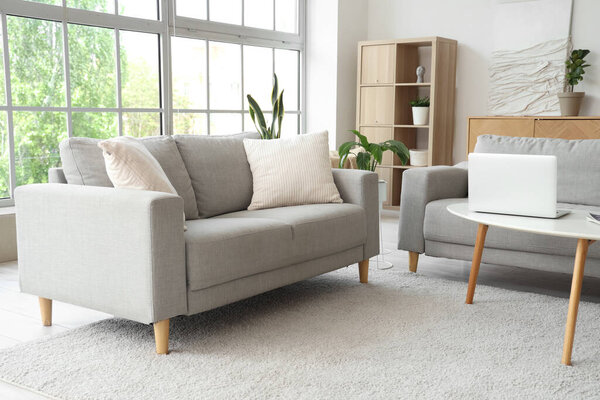 Interior of stylish living room with grey sofas and laptop on table