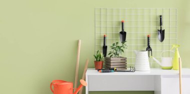 Atölyede yeşil duvarın yanında çivi tahtası ve bahçe aletleri olan çalışma yeri