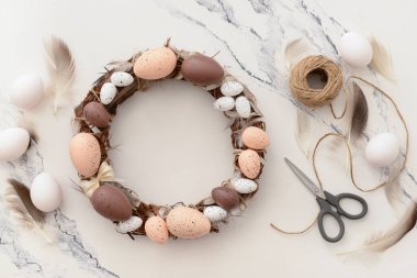 Beyaz masada Paskalya çelengi yapmak için gerekli malzemelerle kompozisyon