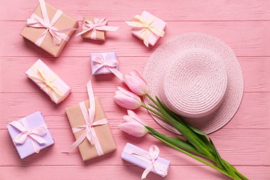 Hediye kutuları, pembe laleler ve pembe ahşap masada hasır şapka. Üst görünüm