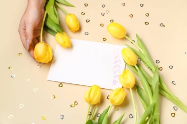 Taze laleli kompozisyon, boş kart ve bej arka planda kadın eli.