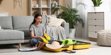 Evde yerde parmak arası terlikleri bavulda toplayan genç bir kadın. Yaz yolculuğu konsepti