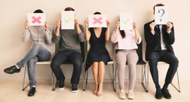 Gençler kapalı koltuklarda otururken farklı işaretler ile kağıt levhalar tutan genç insanlar. İş görüşmesi kavramı