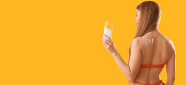 Mayolu ve sarı arka planda güneş kremi sürmüş genç bir kadın.