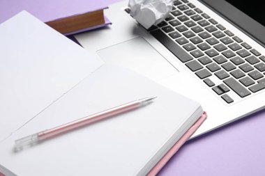 Blank open book, pen and laptop on lilac background, closeup. World Poetry Day celebration