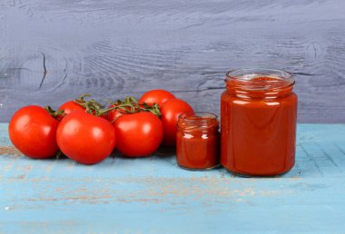 Lezzetli domates ezmeli kavanozlar ve mavi ahşap arka planda taze sebzeler.
