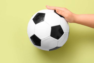 Sarı arka planda futbol topu olan el.