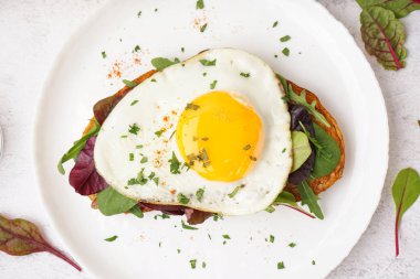 Yağda yumurta ve açık arkaplanda yeşillikler olan lezzetli bir sandviç.