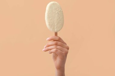 Elinde nefis çikolata kaplı dondurma tutan kadın bej arka planda.