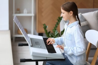 Evde sentezleyici oynayan küçük kız.