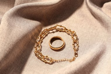 Bej kumaş arka planda güzel bir yüzük ve zincir bilezik.