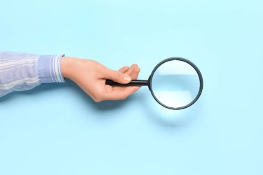 Mavi arka planda büyüteçle kadın eli