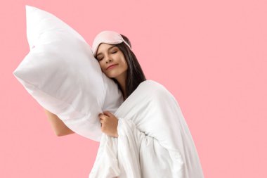 Yumuşak yastıklı ve battaniyeli güzel bir kadın pembe arka planda uyuyor.