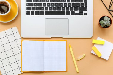 Laptop ve turuncu arka planda bir fincan kahve ve kırtasiye malzemesi.