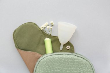 Tekrar kullanılabilir regl pedi, fincanı ve gri arka planda tamponu olan kadının makyaj çantası.