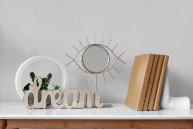 Küçük ayna, kitaplar ve floraryum gri duvarın yanındaki beyaz masada, yakın plan.