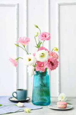 Güzel pembe Eustoma çiçekli vazo, bir tabak badem kurabiyesi ve gri masada bir fincan kahve.