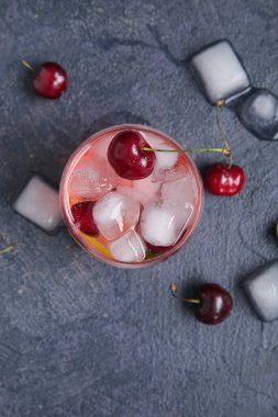 Koyu arkaplanda bir bardak kirazlı limonata ve buz.