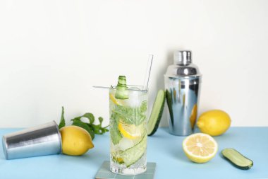 Barmen aletleriyle beyaz duvarın yanındaki mavi masada bir bardak mojito.