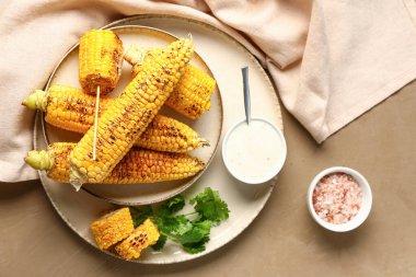 Lezzetli ızgara mısır koçanı ve kahverengi arka planda sos tabağı.