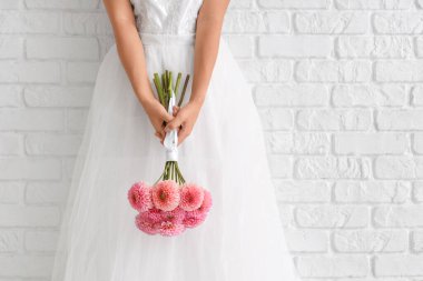 Beyaz tuğla duvarın yanında pembe yıldız çiçekleriyle güzel bir Asyalı gelin, yakın plan.