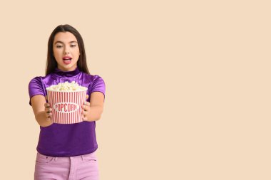 Bej arka planda bir kova patlamış mısırla güzel, şaşırmış genç bir kadın.