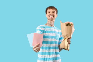 Çiçek buketi ve mavi arka planda zarfları olan mutlu genç adam.