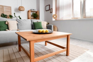 Oturma odasının iç tarafındaki ahşap sehpada limonlu rahat gri kanepe ve tabak.