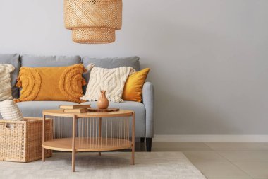 Yastıklı şık gri kanepe, sehpa ve sepet gri duvarın yanında.