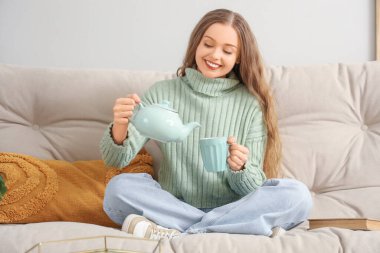 Evdeki kanepede fincana çay dolduran genç kadın.