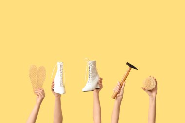 Sarı arka planda çizmeli, çekiçli ve tabanlı kadın elleri var. Ayakkabı tamiri kavramı