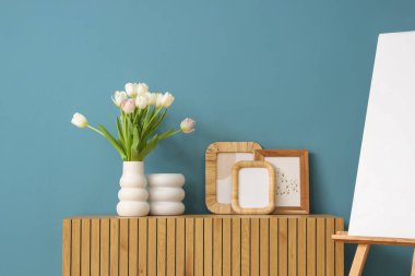 Odada mavi duvarın yanında klozette laleler olan fotoğraf çerçeveleri ve vazolar.