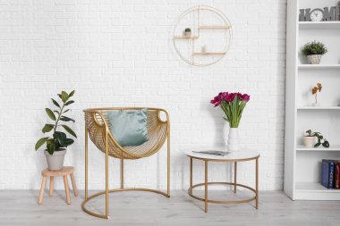 Yastıklı sandalye, sehpa ve beyaz duvarın yanındaki çiçekler.