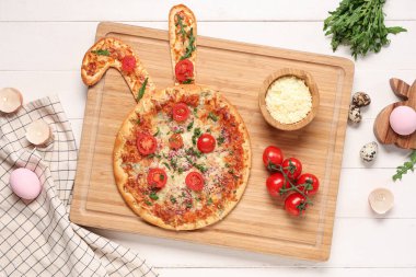 Lezzetli Paskalya pizzası, tavşan kulaklı, yumurtalı, peynirli ve domatesli beyaz ahşap arka planda.