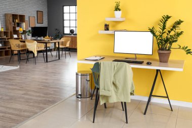 Ofiste sarı duvarın yanında bilgisayar monitörü ve bitkileri olan modern işyeri