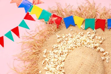 Pembe arka planda Festa Junina kutlamaları için şık hasır şapka, patlamış mısır ve renkli bayraklar, yakın plan