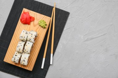 Gri grunge arka planında lezzetli suşi dürümleri, yemek çubukları ve bambu paspası olan tahta.
