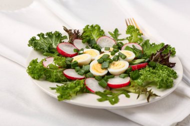 Bir tabak taze sebzeli lezzetli salata ve arka planda kaynamış bıldırcın yumurtası.