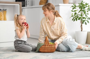 Mutfakta yerde oturan küçük bir kız ve meyve sepetli dadı.