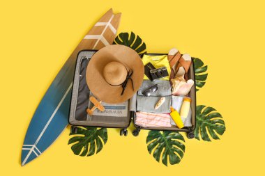 İçinde giysiler, plaj aksesuarları, vibratör ve sarı arka planda palmiye yaprakları olan valizi aç.