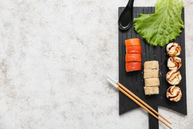 Lezzetli suşi ruloları, yemek çubukları ve beyaz grunge arka planda marul.