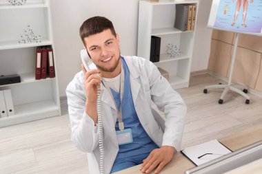 Erkek resepsiyonist hastanede telefonla konuşuyor.