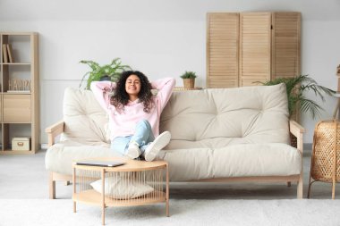 Genç Afro-Amerikalı kadın evdeki kanepede dinleniyor.