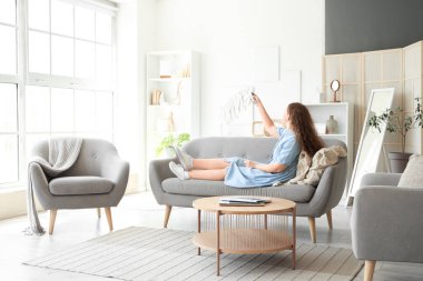 Evdeki kanepede oturan klimalı uzaktan kumandalı genç bir kadın.