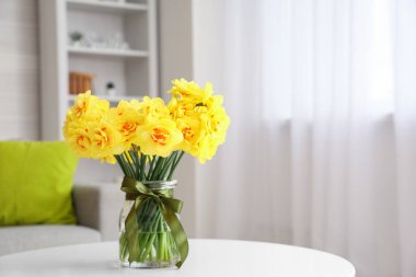 Oturma odasındaki sehpanın üzerinde nergis çiçekleri olan vazo.