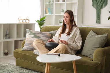 Evdeki yeşil koltukta glukofon çalan genç bir kadın.