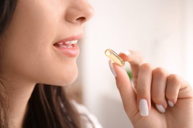 Beautiful young happy woman with healthy fish oil capsule at home, closeup