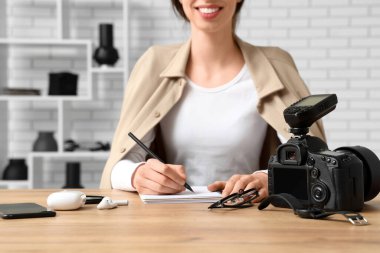 Profesyonel ekipmanlarla masada otururken deftere yazı yazan kadın fotoğrafçı.