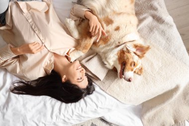 Avustralya çoban köpeği olan genç bir kadın yatağında yatıyor.