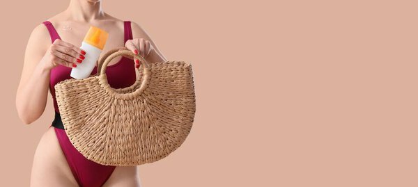 Young woman with sunscreen cream and beach bag on beige background with space for text